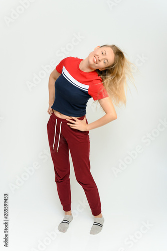 Full length studio portrait of a pretty young happy blonde woman in a tracksuit on a white background. He smiles, talks, shows with his hands, moves, shows emotions.