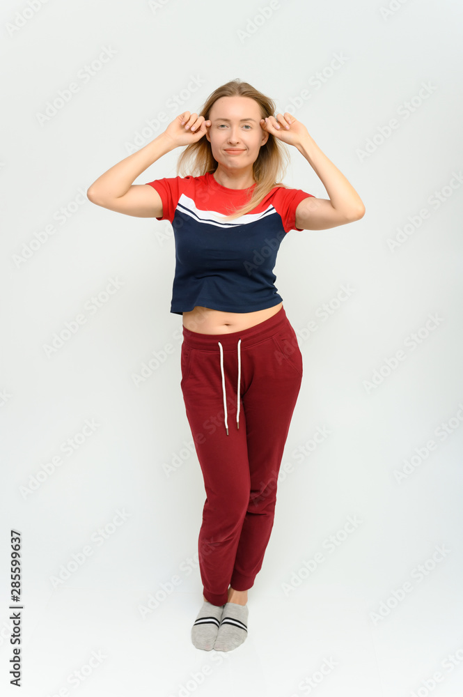 Full length studio portrait of a pretty young happy blonde woman in a tracksuit on a white background. He smiles, talks, shows with his hands, moves, shows emotions. Full length studio portrait of a pretty young happy blonde woman in a tracksuit on a white background. He smiles, talks, shows with his hands, moves, shows emotions.
