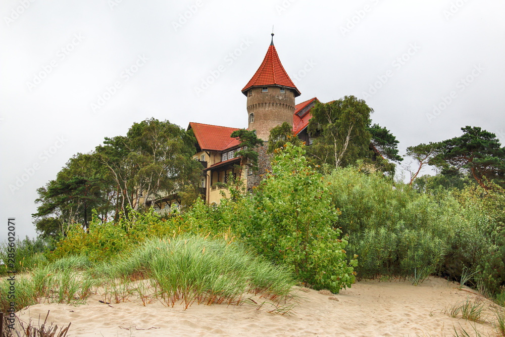 LEBA, POLAND - JULY 23, 2019: Neptun Castle on the Baltic Sea in Leba, Poland. In 1903 almost on the beach , the build of this interesting architectonically building was begun (completed in 1907). - obrazy, fototapety, plakaty 