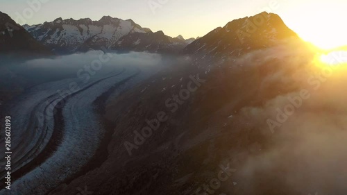 Aerial, pan, drone shot, of sunrise above clouds, revealing the Aletsch glacier, in the middle of snowy mountain peaks, , on a sunny, summer morning, in the Swiss alps of Valais, Switzerland photo