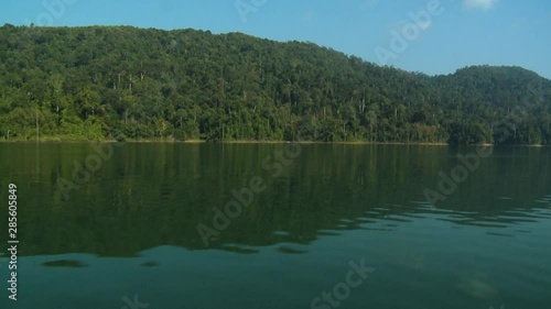 wide low-angle boat sailing shot of a highland forest range below a clear blue sky, and its symmetrical reflection on the  calm waters of Lake Temenggor, Gerik, KL, Malaysia photo