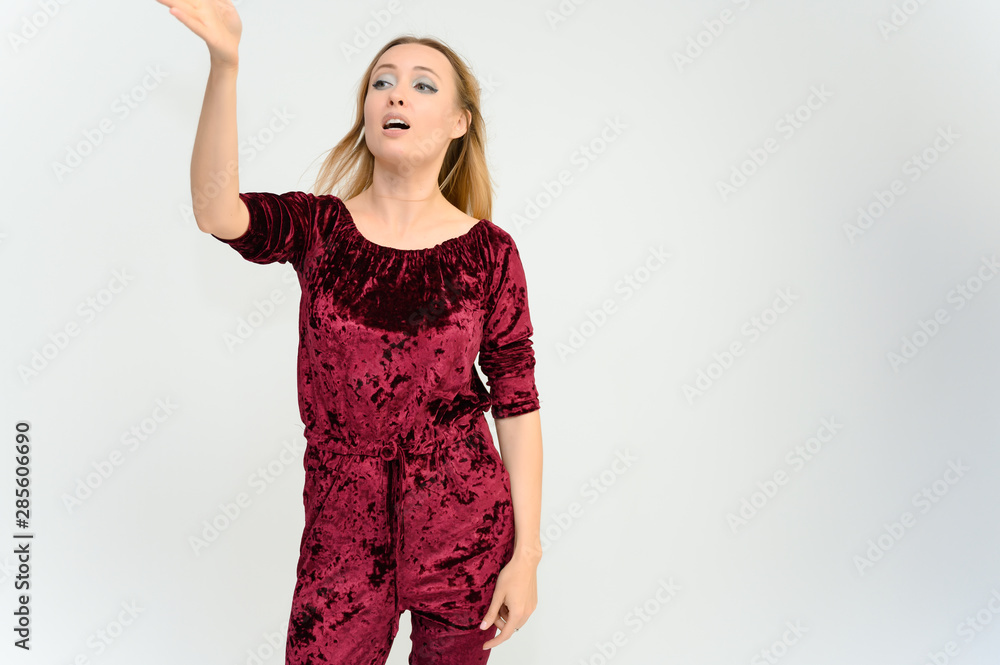 Studio knee-length portrait of a pretty beautiful young happy blonde woman on a white background in red overalls. Smiling, talking, showing emotions. Studio knee-length portrait of a pretty beautiful young happy blonde woman on a white background in red overalls. Smiling, talking, showing emotions.