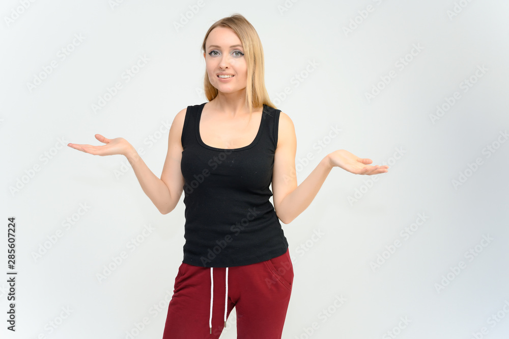 Studio knee-length portrait of a pretty beautiful young happy blonde woman on a white background in a black t-shirt and red trousers. Smiling, talking, showing emotions. Studio knee-length portrait of a pretty beautiful young happy blonde woman on a white background in a black t-shirt and red trousers. Smiling, talking, showing emotions.