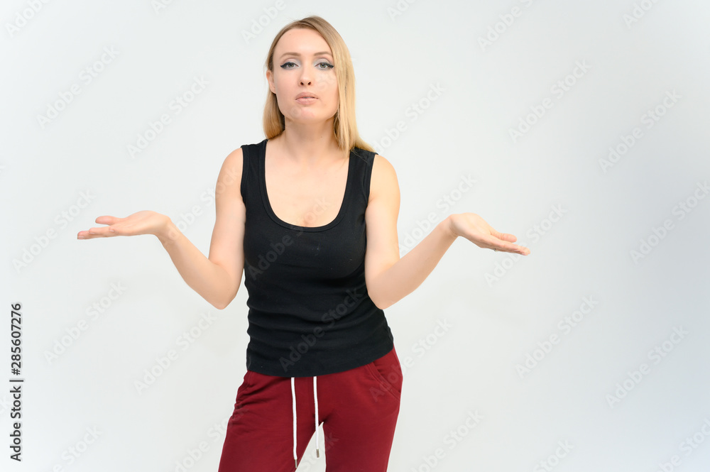 Studio knee-length portrait of a pretty beautiful young happy blonde woman on a white background in a black t-shirt and red trousers. Smiling, talking, showing emotions. Studio knee-length portrait of a pretty beautiful young happy blonde woman on a white background in a black t-shirt and red trousers. Smiling, talking, showing emotions.