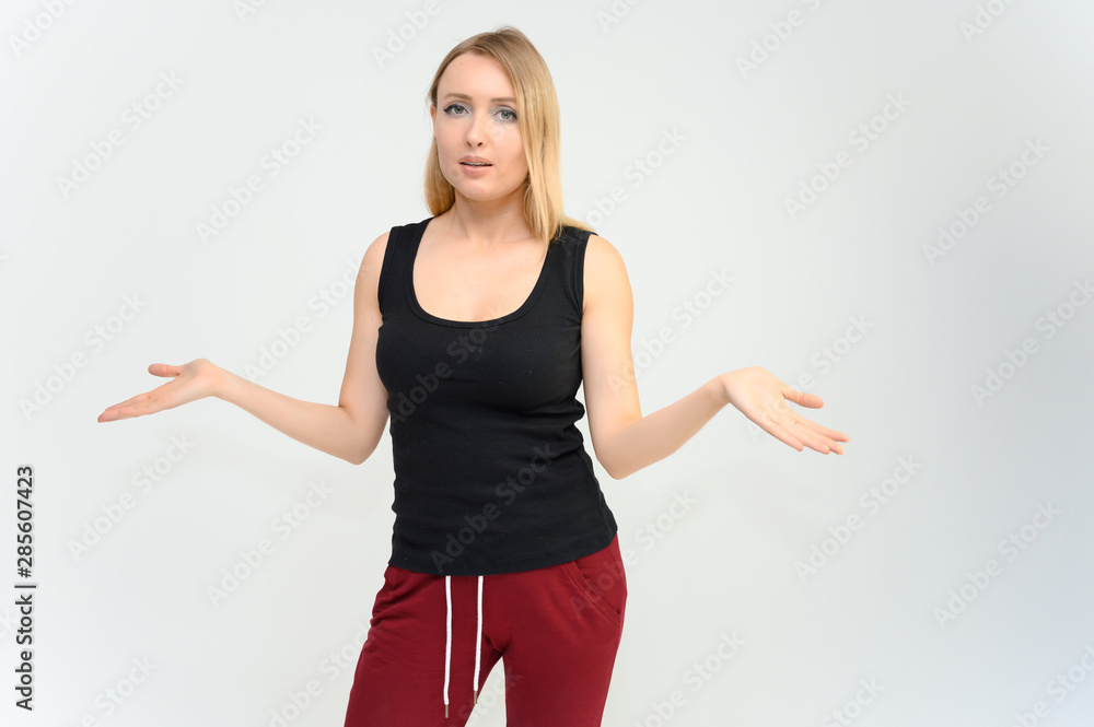 Studio knee-length portrait of a pretty beautiful young happy blonde woman on a white background in a black t-shirt and red trousers. Smiling, talking, showing emotions. Studio knee-length portrait of a pretty beautiful young happy blonde woman on a white background in a black t-shirt and red trousers. Smiling, talking, showing emotions.