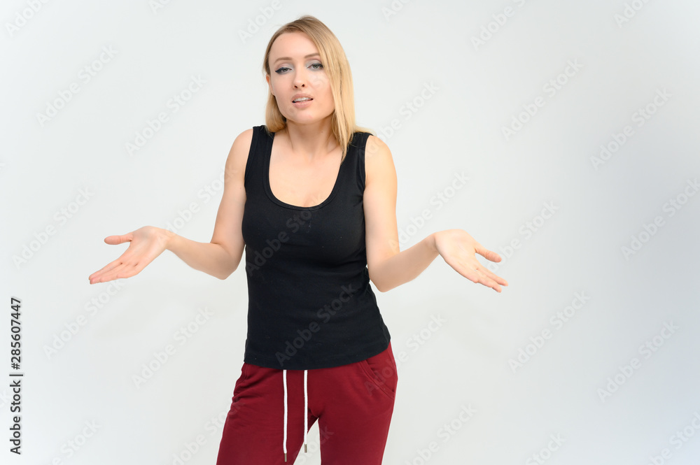 Studio knee-length portrait of a pretty beautiful young happy blonde woman on a white background in a black t-shirt and red trousers. Smiling, talking, showing emotions. Studio knee-length portrait of a pretty beautiful young happy blonde woman on a white background in a black t-shirt and red trousers. Smiling, talking, showing emotions.