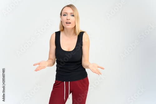 Studio knee-length portrait of a pretty beautiful young happy blonde woman on a white background in a black t-shirt and red trousers. Smiling, talking, showing emotions.