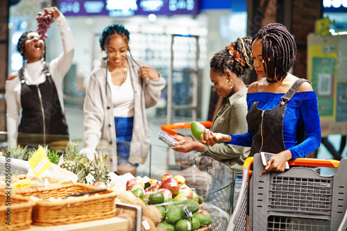 Group of african womans with shopping cart buying exotic fruits in grocery store supermarket.
