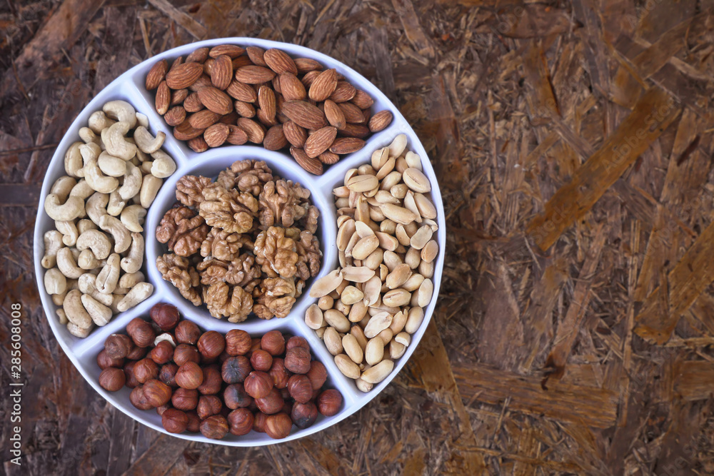 Nuts are part of a healthy diet . Set of nuts - walnut , cashew , peanuts , hazelnuts , almonds on a plate divided into portions . On a brown textured background. Nuts are part of a healthy diet . Set of nuts - walnut , cashew , peanuts , hazelnuts , almonds on a plate divided into portions . On a brown textured background.