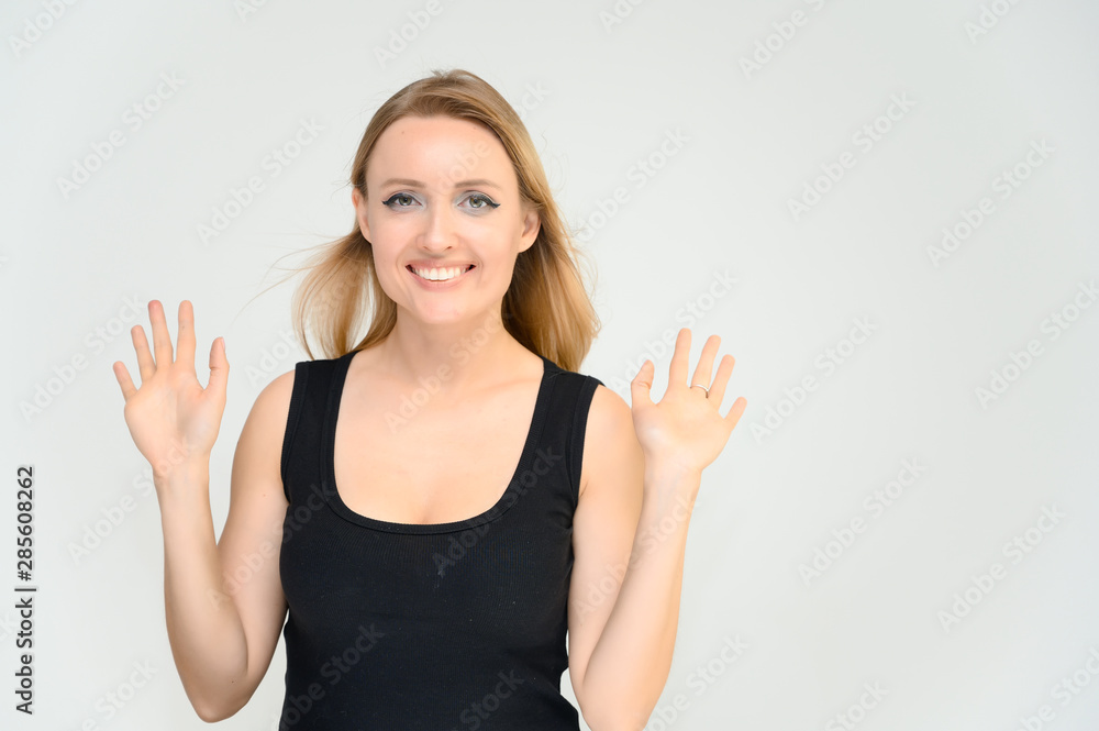 Fototapeta premium Studio waist-length photo portrait of a pretty beautiful young happy blonde woman on a white background in a black t-shirt. Smiling, talking, showing emotions.
