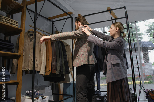 Cuadro en lienzo Girl stylist in a clothing store helps a young guy to pick up things