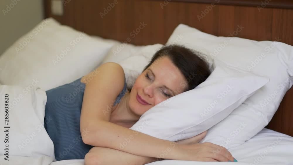 Close-up of woman sleeping sweetly wakes up and happy stretching in white bed to bed in the bedroom, slow motion Close-up of woman sleeping sweetly wakes up and happy stretching in white bed to bed in the bedroom, slow motion