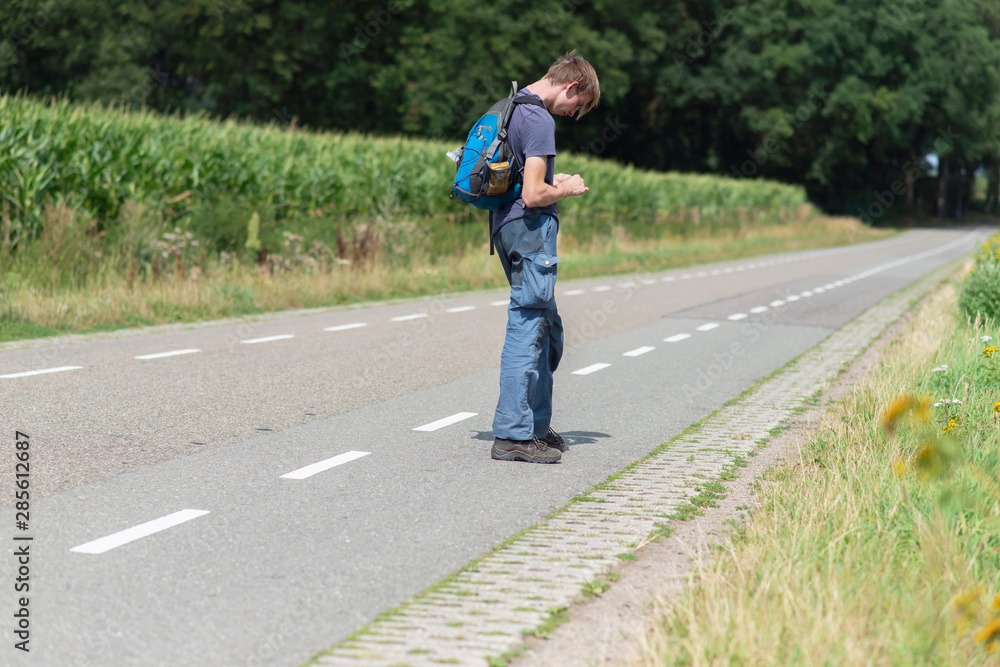 Fototapeta premium Young man with backpack on country road in summer.