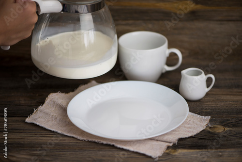 milk is pouring from a glass jug and a white empty plate on an old wooden background