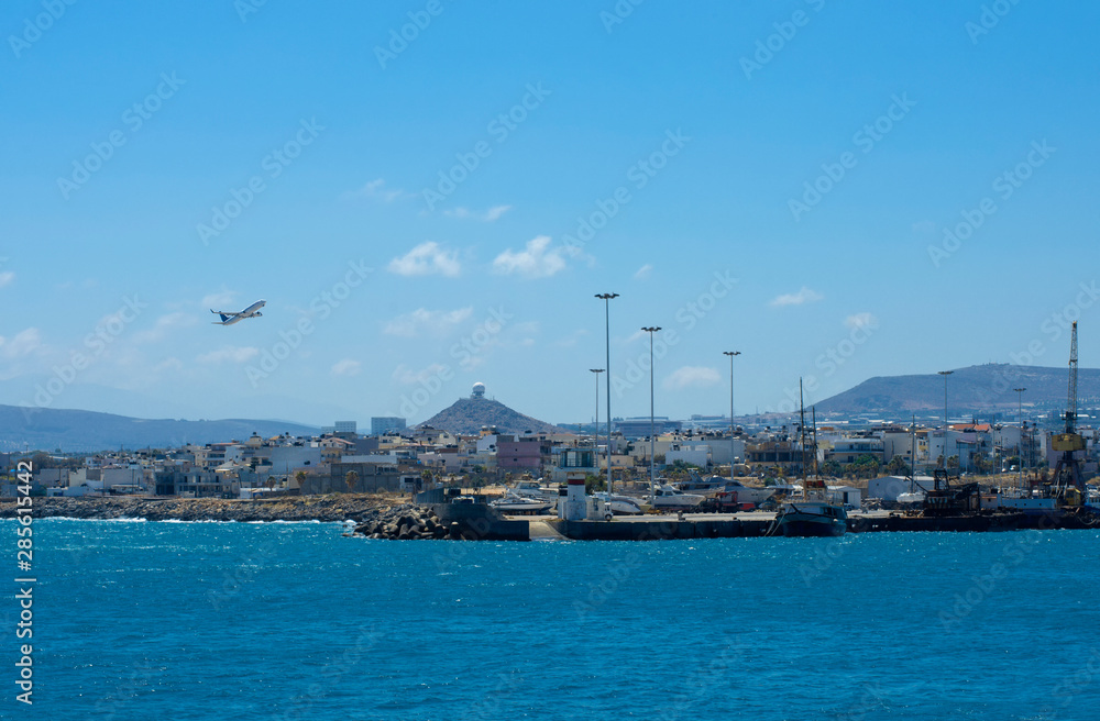 Airliner takes off over the port of Heraklion in clear weather on a hilly background with the command and control center