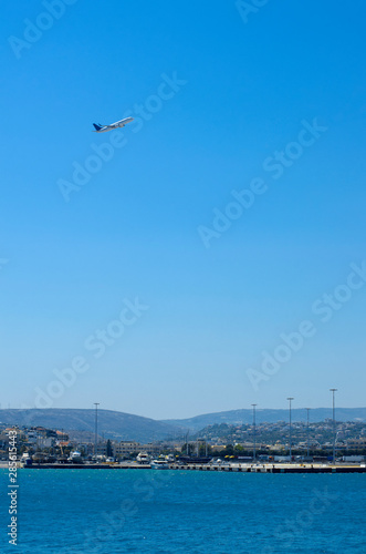 The plane is gaining altitude in the blue sky over the port area of Heraklion (Greece)