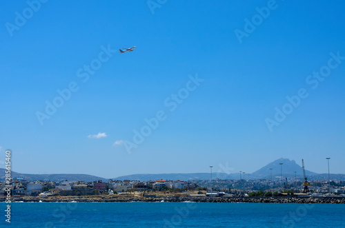 Airliner in the blue sky over the Harbor of Heraklion and in the distance the top of the mountain and hills