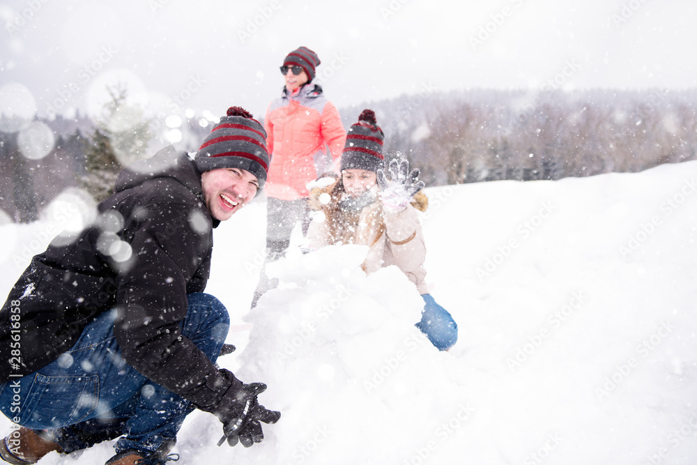 group of young people making a snowman - obrazy, fototapety, plakaty 