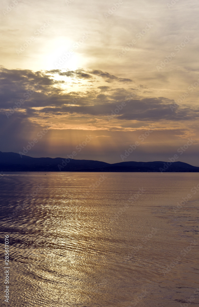 Greece, the Aegean sea. A view from a ferry sailing at sunset. The sunset over the distant isle of Kythnos. An atmospheric sky. Natural beauty. Nature, open air and calmness.