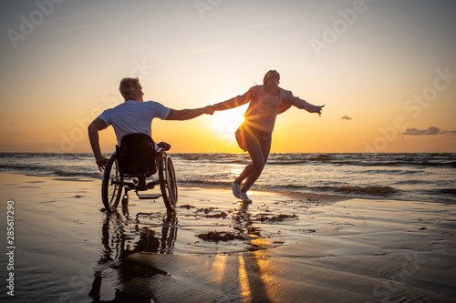Handicapped man in wheelchair and his girlfriend on a beach at sunset photo