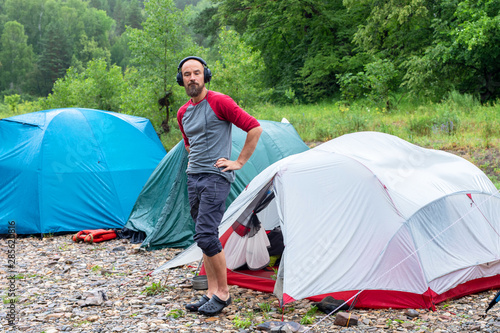 man in a campground with headphones. a tourist, traveler or explorer in his spare time listening to music near a tent