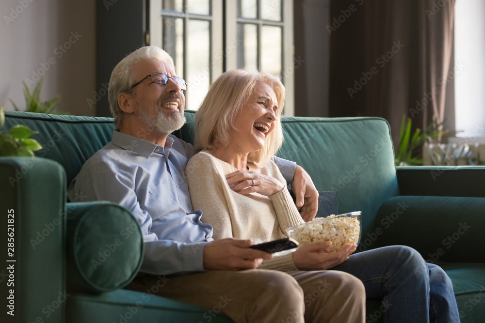 Cheerful old couple holding remote control laughing watching funny tv