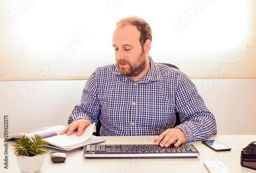 Young man with plaid shirt sitting in an office working on an important project.