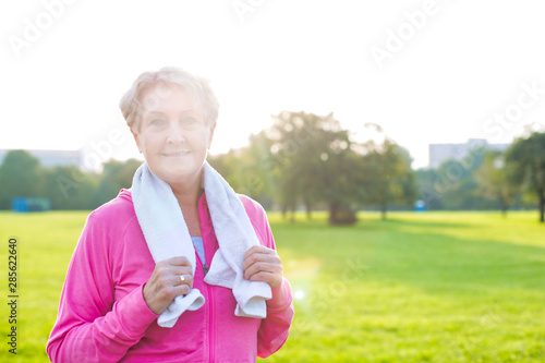 Confident senior woman with towel standing in park