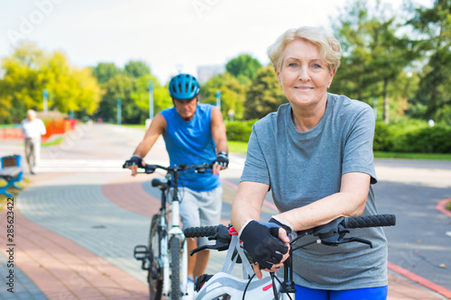 Confident senior woman leaning on bicycle in park