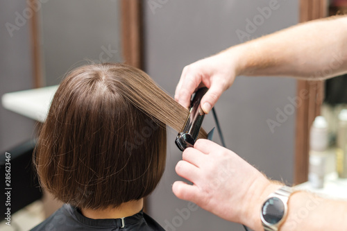 Hairdresser straightening brown hair with hair irons.