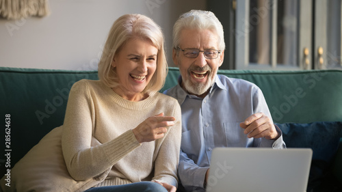 Happy old couple looking at laptop laughing watching comedy movie