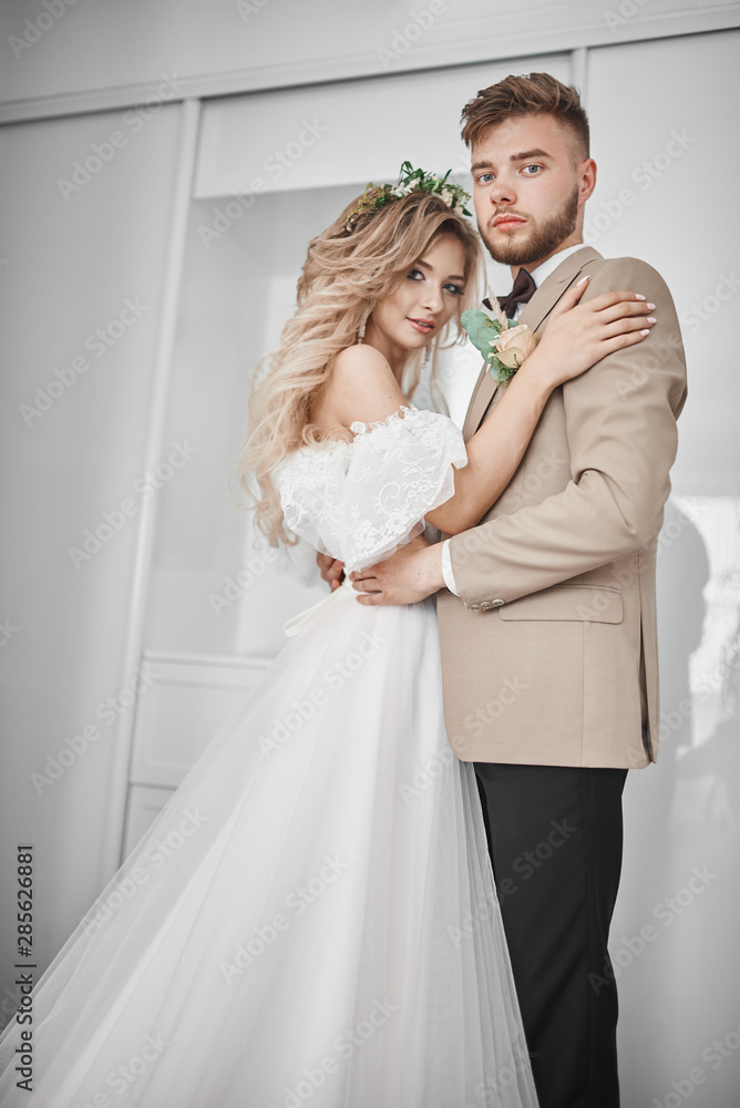 Wedding photo session at the hotel. Tender and bright photos. Sensual bride and stylish groom are standing by the bright window.