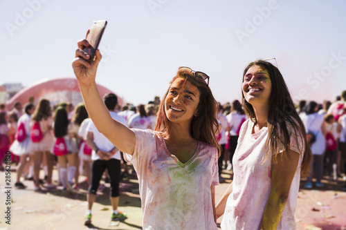 Portrait of a happy young women taking selfie on mobile phone during holi festival