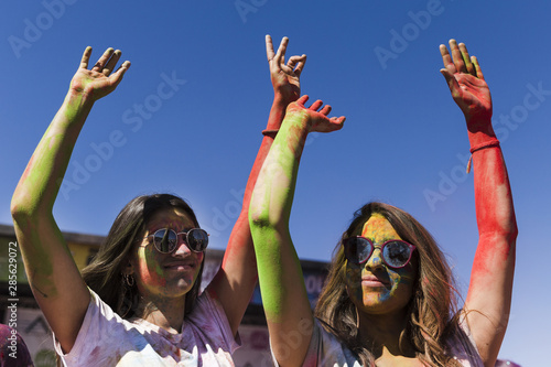 Young women wearing sunglasses enjoying the holi festival against blue sky © Freepik