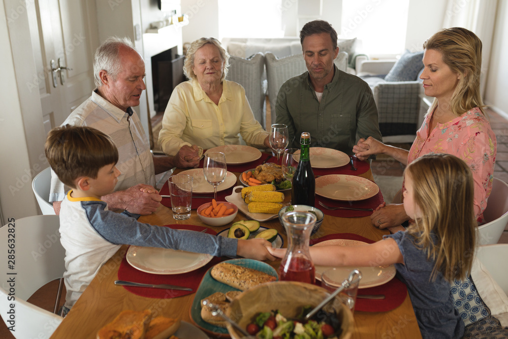 Family praying together before having meal on dining table