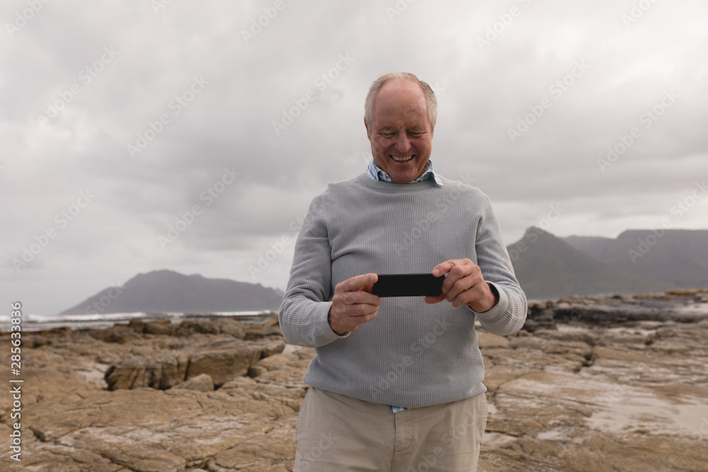 Senior man reviewing photos on mobile phone at beach