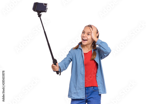 Portrait of beautiful happy teen girl making selfie with stick. Teenager posing to smartphone on selfie stick, isolated on white background. Child taking selfie on mobile phone for social network.