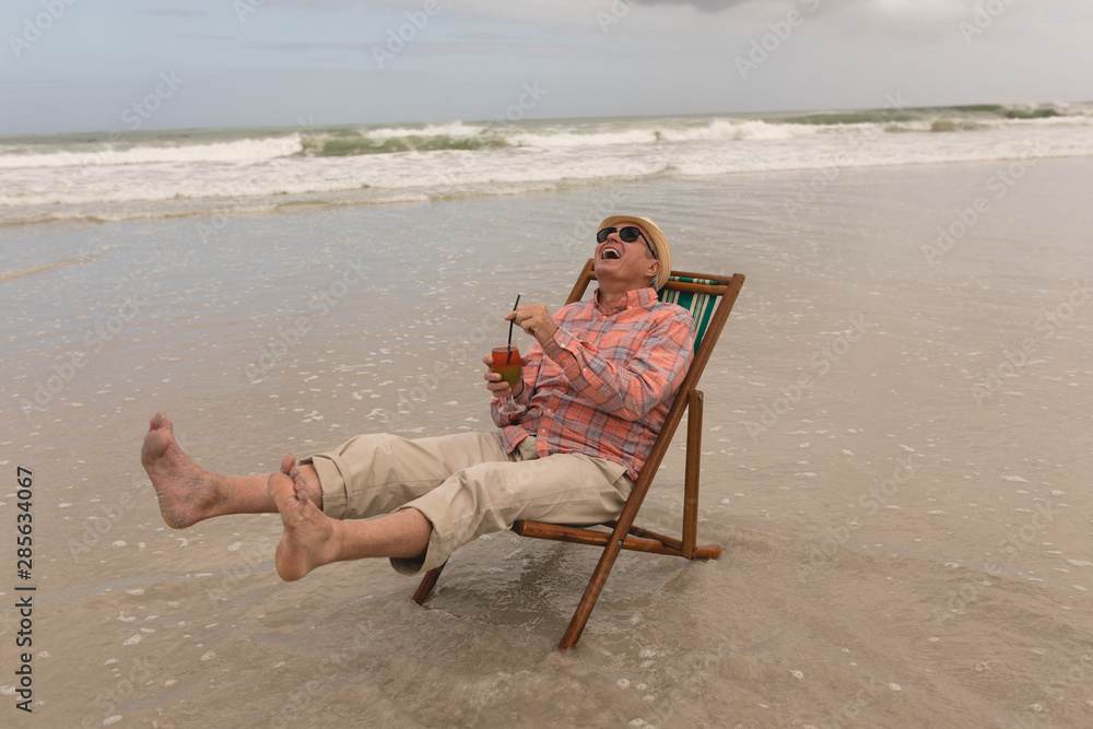 Senior man having cocktail drink while relaxing in a sun lounger 
