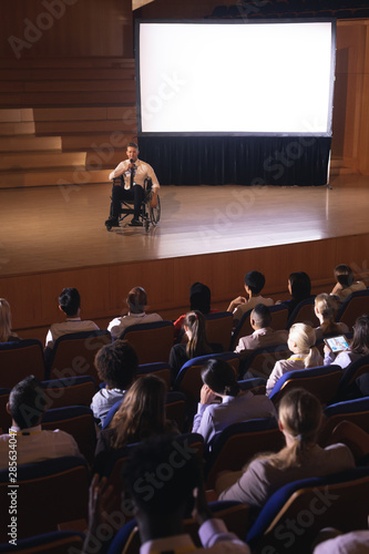 Businessman sitting on a wheelchair and giving presentation to the audience 