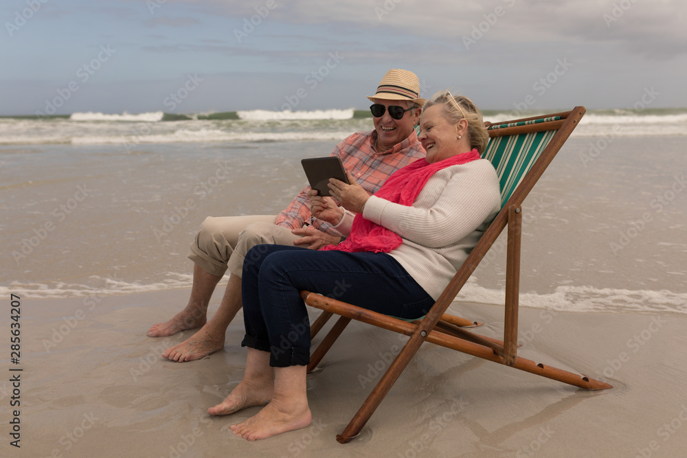 Senior couple using digital tablet while relaxing in a sun lounger