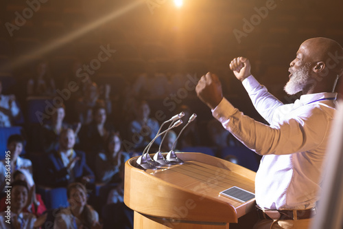 Quadro su tela Businessman standing near podium and giving speech to the audience in the audito