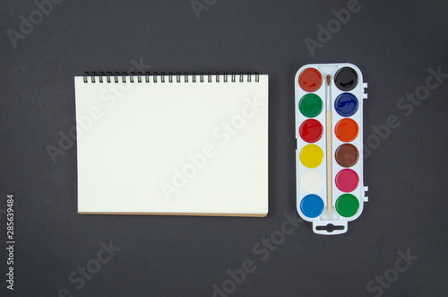 Flat lay mockup back to school concept, frame with blank spiral notebook and watercolor paints on a blackboard background