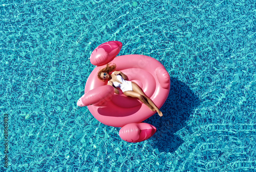 Beautiful  sexy woman inflatable giant pink flamingo float mattress in blue swimming pool with text space. Summer vibes tourist