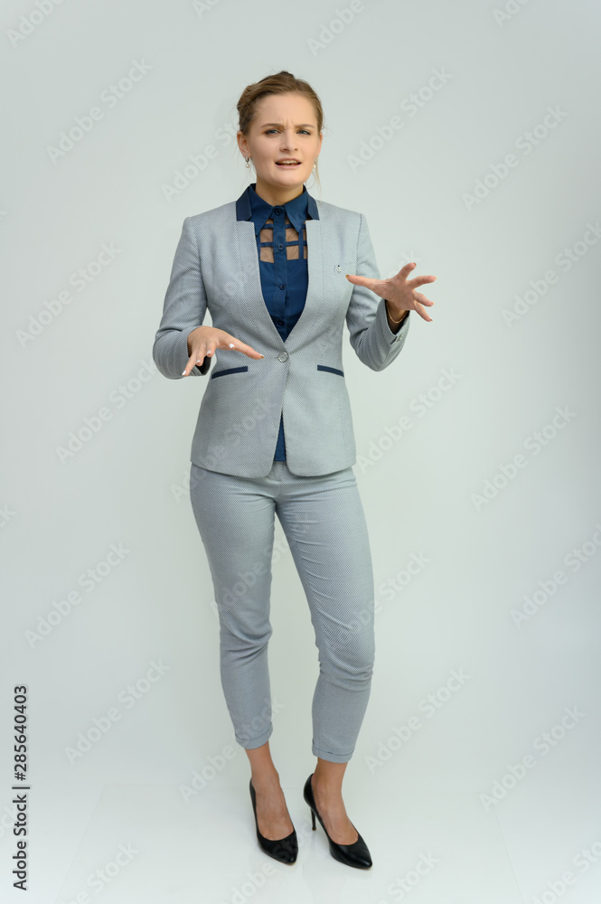 Full length studio portrait of a pretty young woman girl in a business suit on a white background. He stands right in front of the camera, explains, shows hands with emotions. Full length studio portrait of a pretty young woman girl in a business suit on a white background. He stands right in front of the camera, explains, shows hands with emotions.