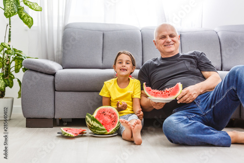grandfather and granddaughter eat watermelon at home