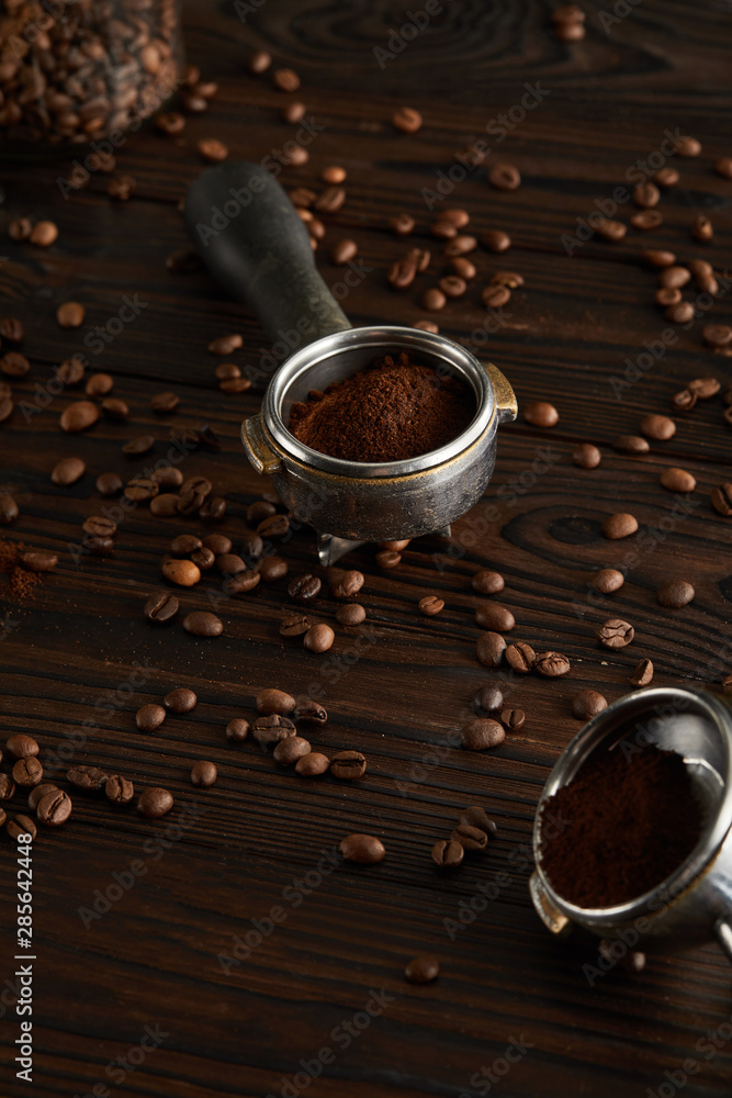 Naklejka premium Portafilters with ground coffee on dark wooden surface with coffee beans