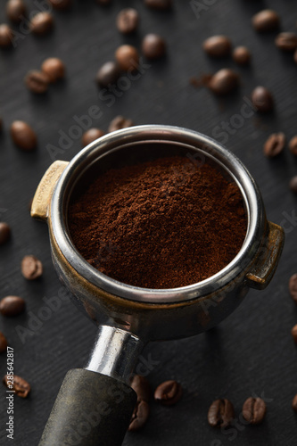 Portafilter with fresh ground coffee on dark wooden surface with coffee beans