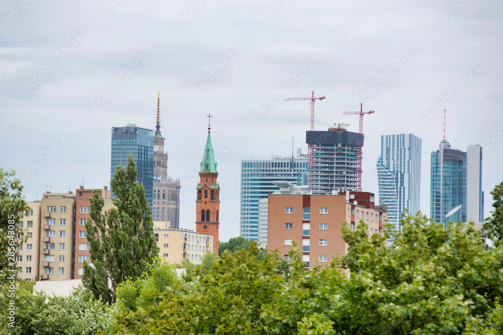 Construction taking place in Warsaw, Poland with old buildings and green trees in the foreground