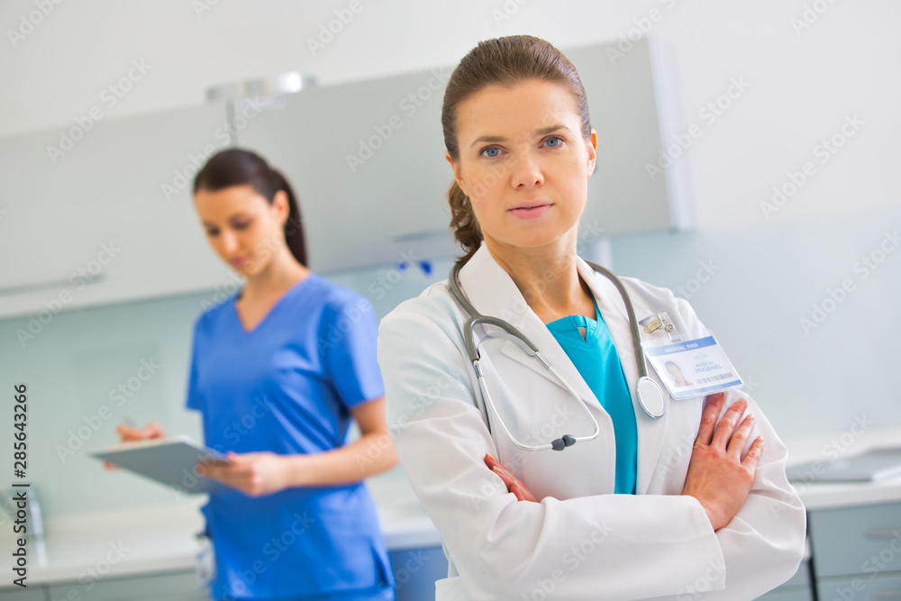 Portrait of confident doctor standing against nurse at clinic Portrait of confident doctor standing against nurse at clinic
