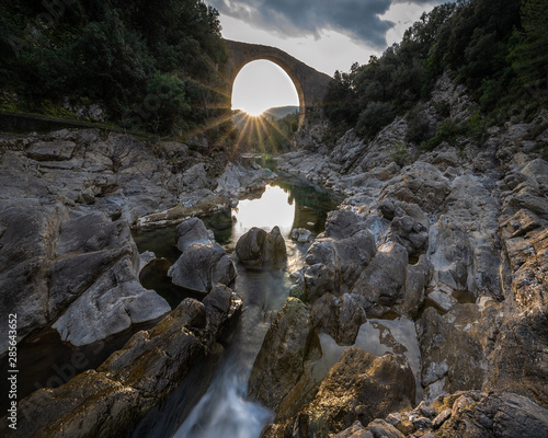 River between rocks towards a beautiful bridge, sunset sun stars